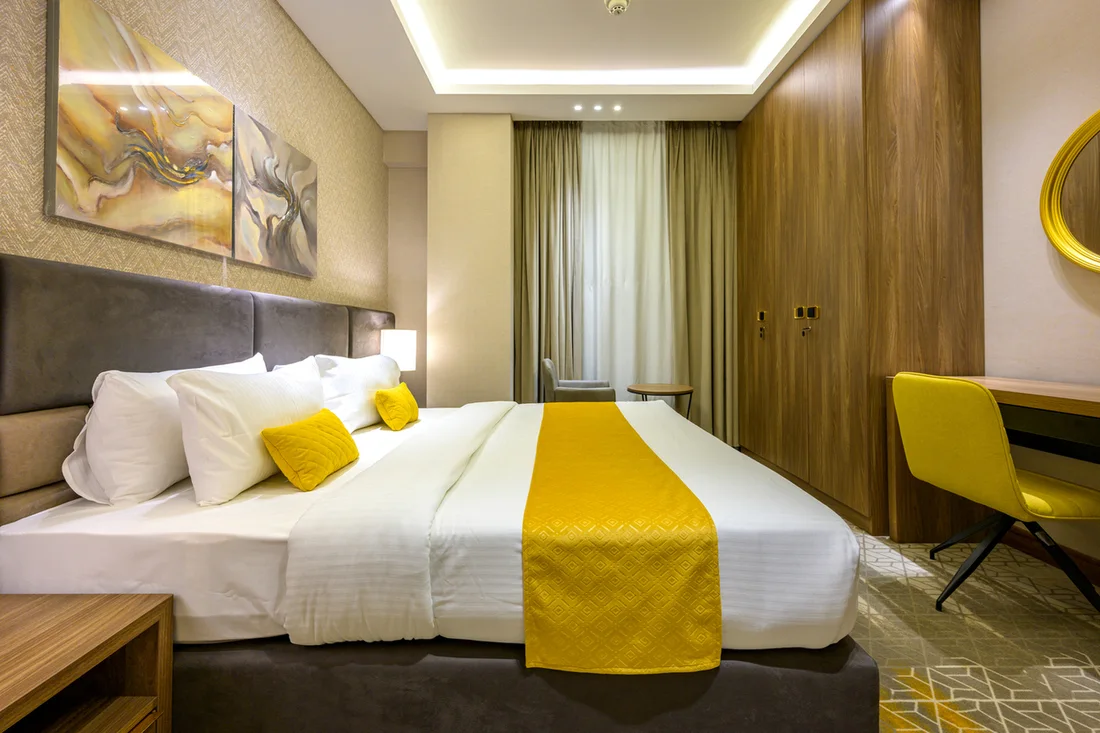 Abraj INN Suites, Doha Hotels: king bed with a yellow runner, full-height wardrobe wall and a desk with a yellow chair