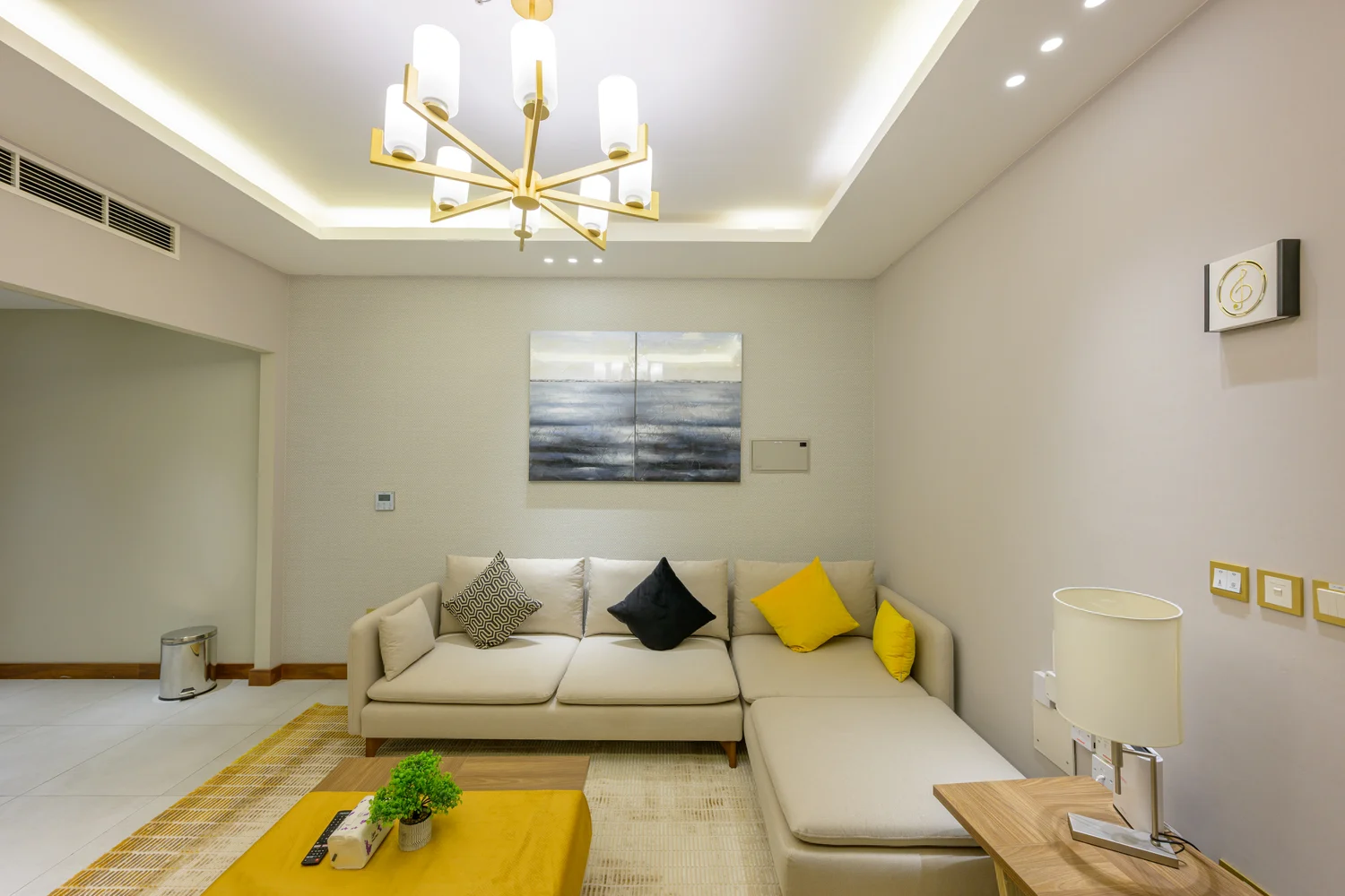Abraj INN Suites, Doha Hotels: cream corner sofa with yellow cushions, a mustard coffee table and a gold chandelier