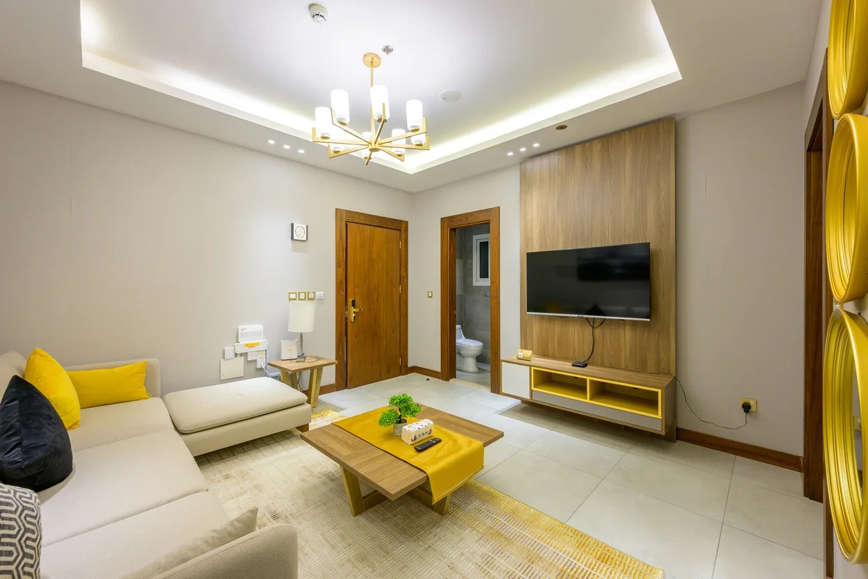 Abraj INN Suites, Doha Hotels: cream L-shaped sofa, wall-mounted TV on a walnut panel and a gold chandelier