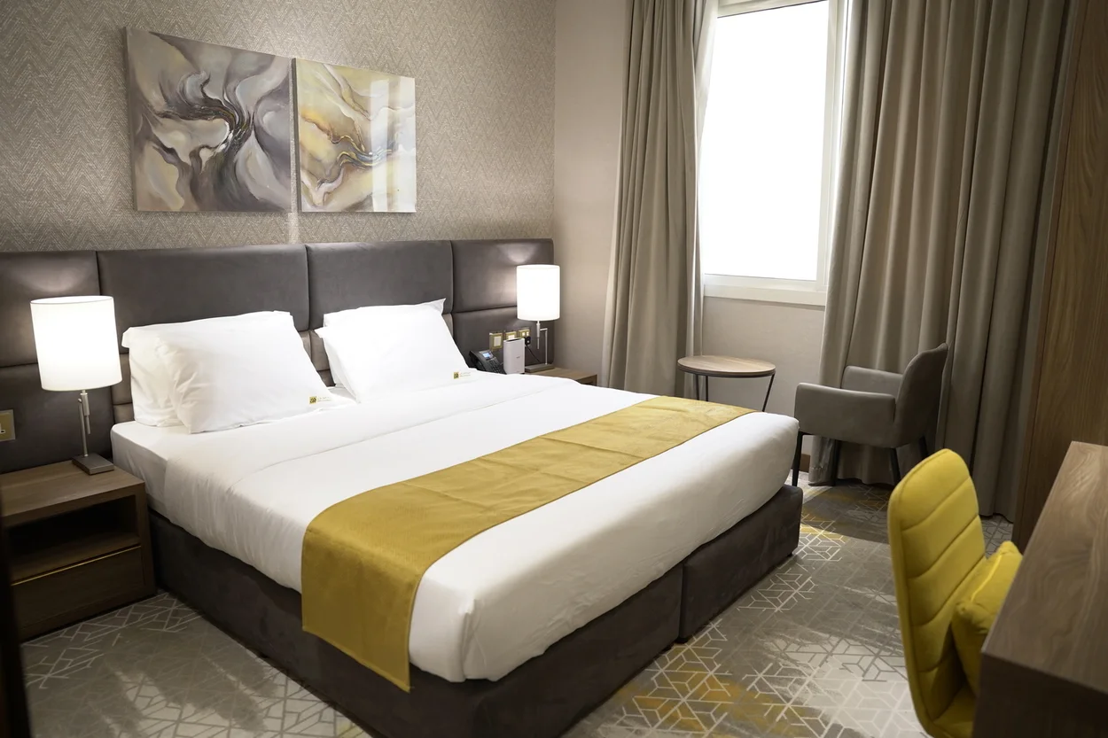 Abraj INN Suites, Doha Hotels: suite bedroom with a twin-joined king bed, bedside lamps, an armchair and a desk chair