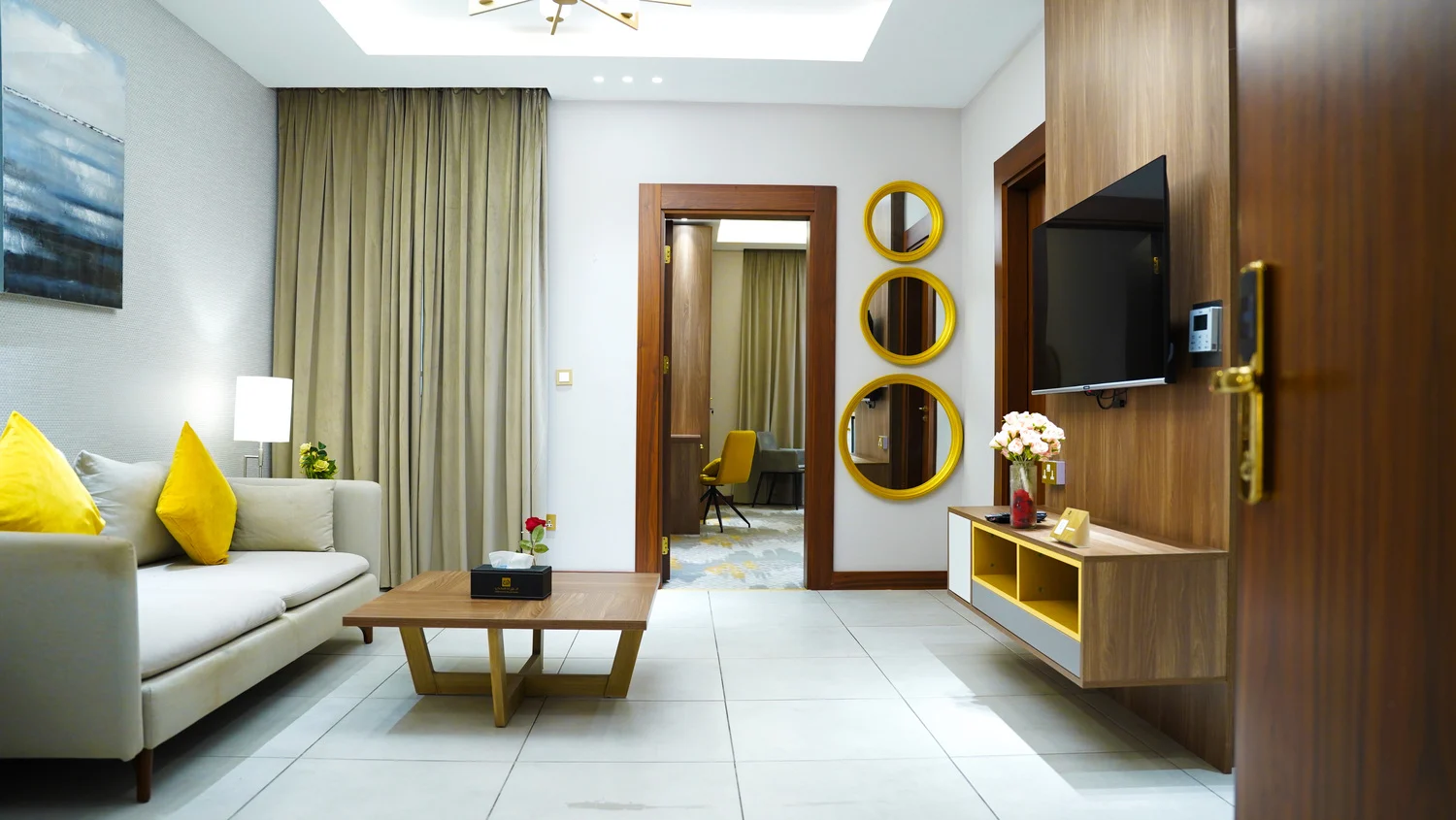 Abraj INN Suites, Doha Hotels: suite living room with a cream sofa, wall-mounted TV and the bedroom door open behind