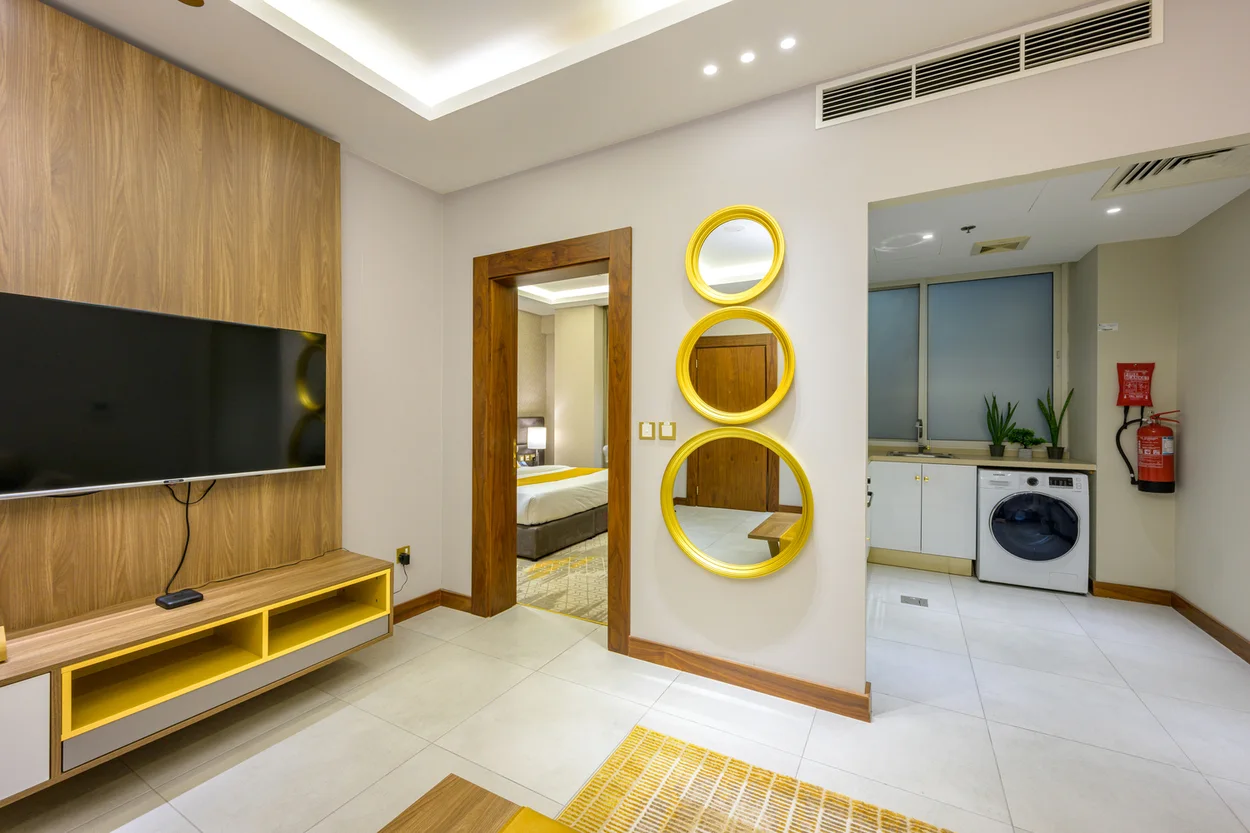 Abraj INN Suites, Doha Hotels: suite living area with a wall-mounted TV, open bedroom doorway and kitchenette alcove