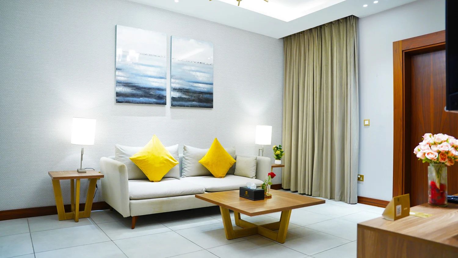 Abraj INN Suites, Doha Hotels: suite sitting room with a cream sofa, yellow cushions, two canvases and table lamps