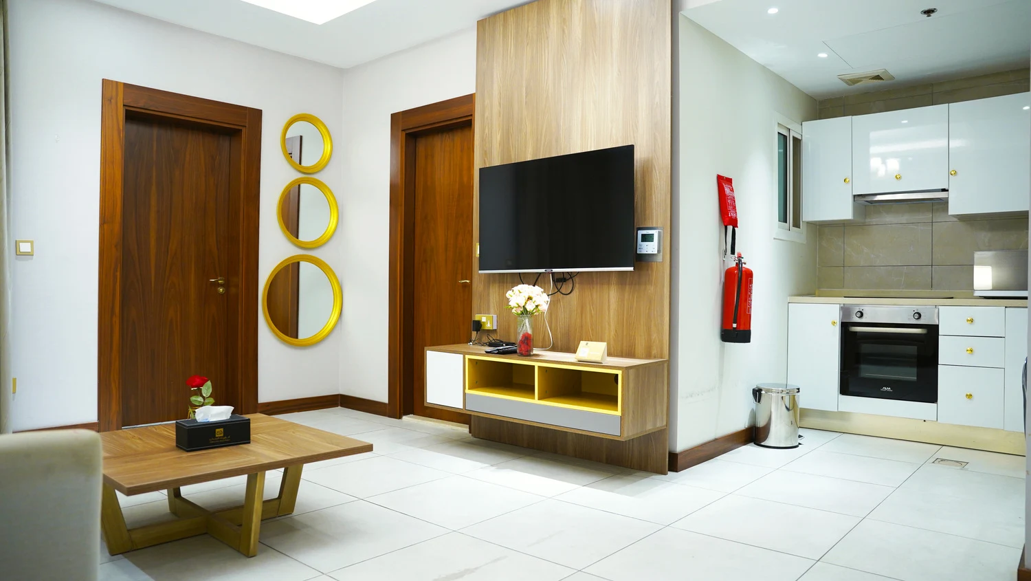 Abraj INN Suites, Doha Hotels: open-plan living area, round gold mirrors, wall-mounted TV and a kitchenette beyond