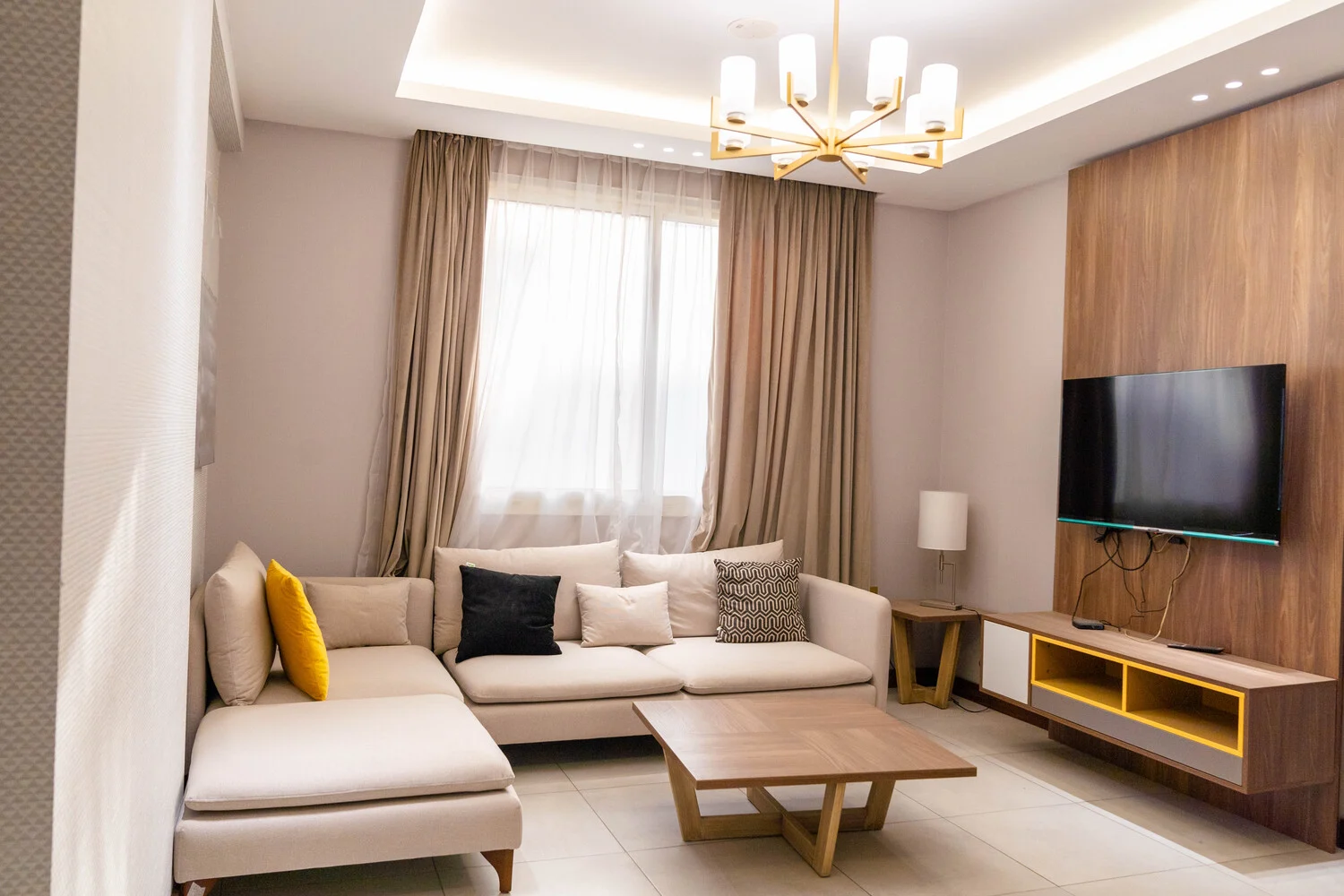 Abraj INN Suites, Doha Hotels: cream L-shaped sofa, oak coffee table, wall-mounted TV and a gold chandelier