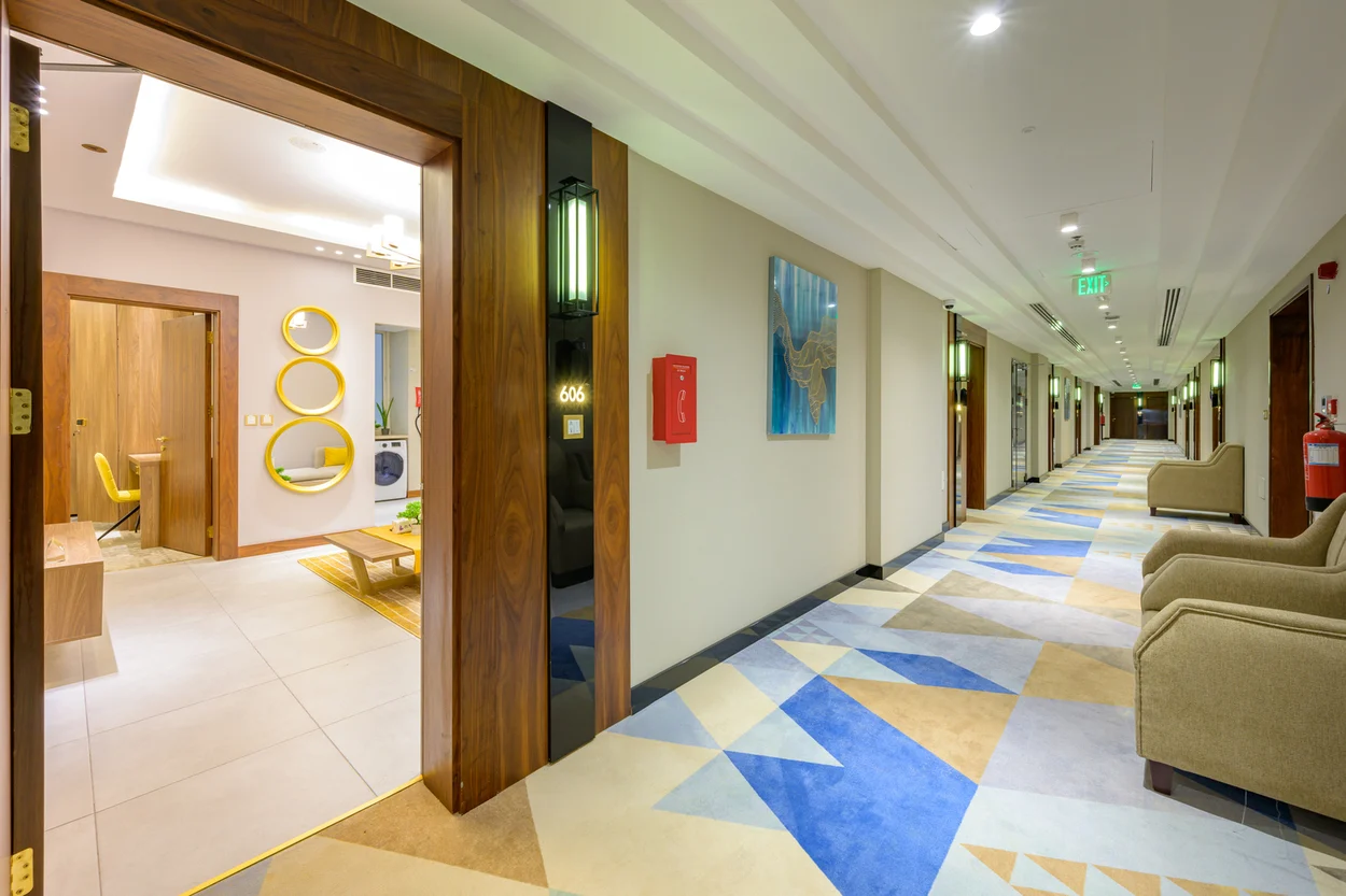 Abraj INN Suites, Doha Hotels: guest-floor corridor with patterned carpet, lit sconces and room 606's door open to a suite.