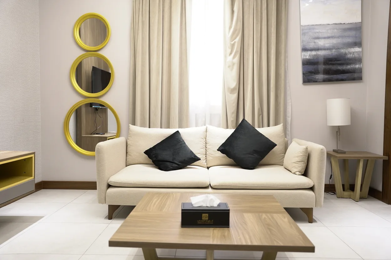 Abraj INN Suites, Doha Hotels: cream sofa, round gold-framed mirrors, an oak coffee table and a bright curtained window.