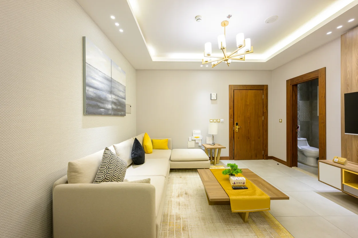 Abraj INN Suites, Doha Hotels: suite lounge with a long cream sofa, wooden coffee table, TV panel and gold chandelier