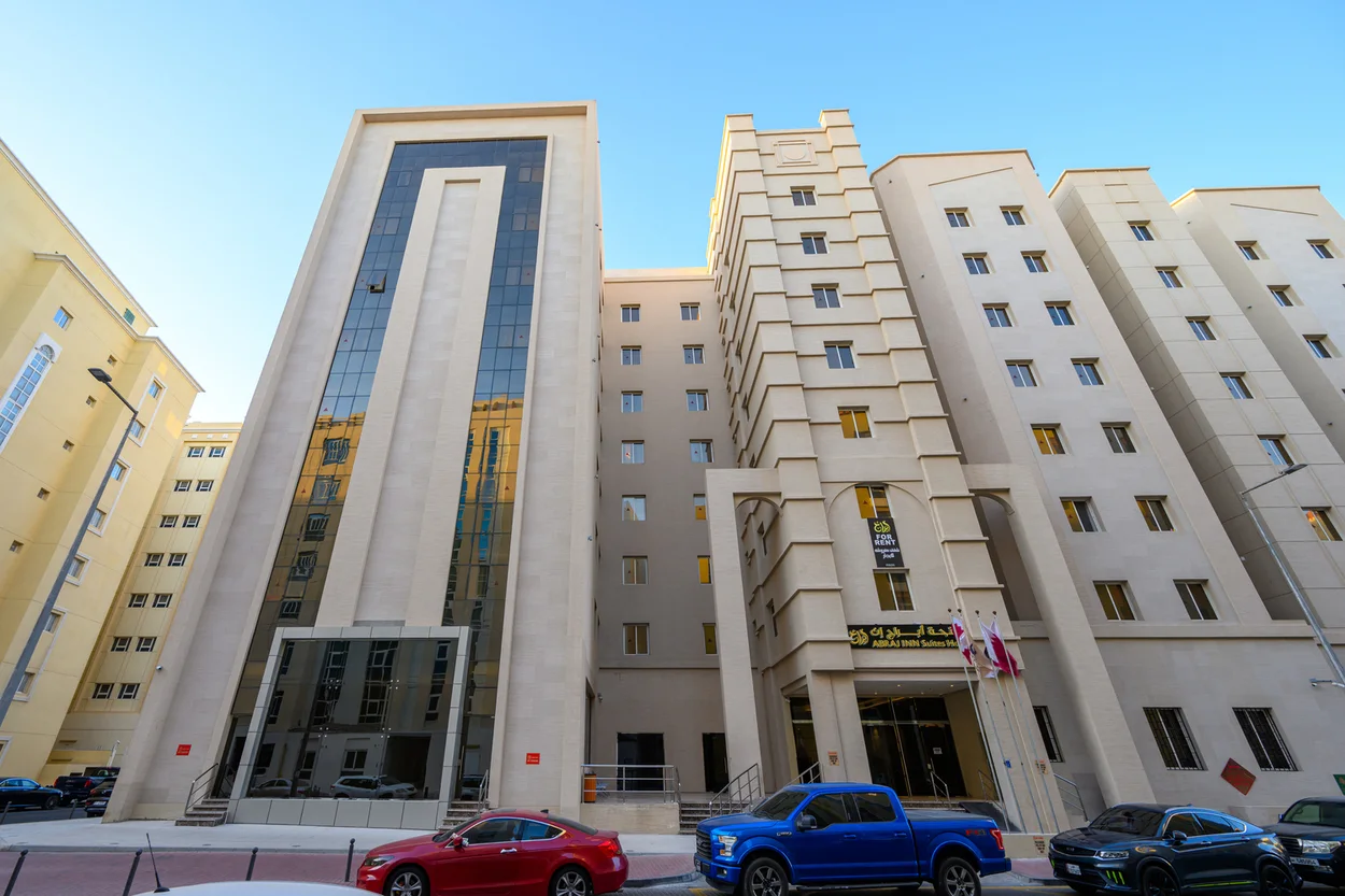 Abraj INN Suites, Doha Hotels: cream stone building from the street, glass stair tower, balconies and flags by the entrance